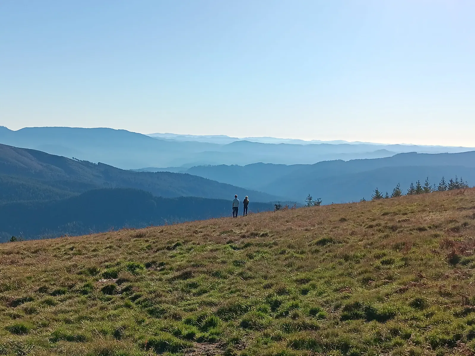 Two people on a grassy ridge above layered blue Oregon mountains