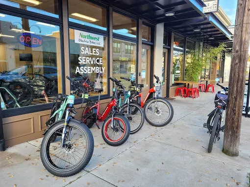 E-bikes lined up outside the Northwest Electric Bikes storefront on 1st Avenue SE in Albany, window lettered Sales Service Assembly
